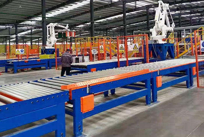 Automated plant floor with white robotic palletizing arms and blue roller conveyors behind orange safety railings.